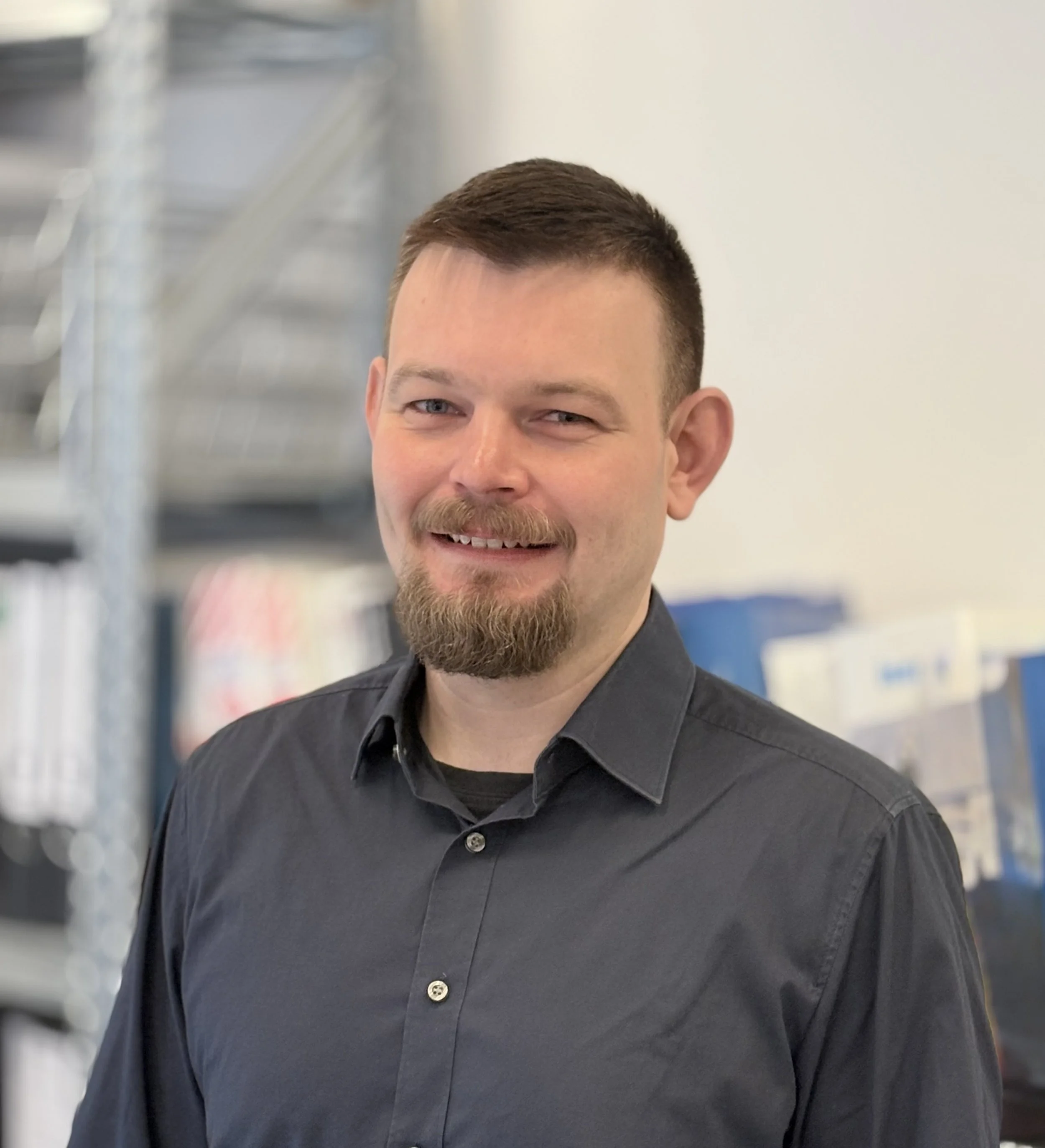 Mann sitzt an einem Schreibtisch in einem Raum mit Bücherregalen im Hintergrund.