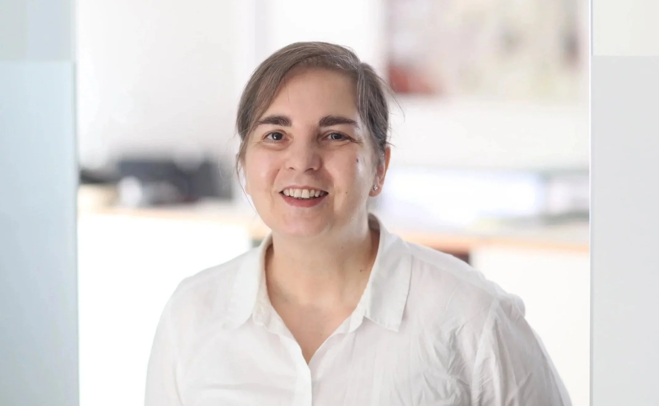 Eine lächelnde Frau in weißem Hemd schaut durch eine Scheibe.