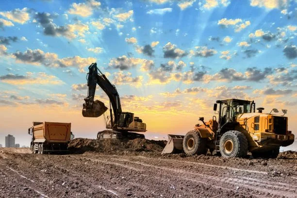 Construction site with excavator and dump truck at sunrise, working on dirt excavation.
