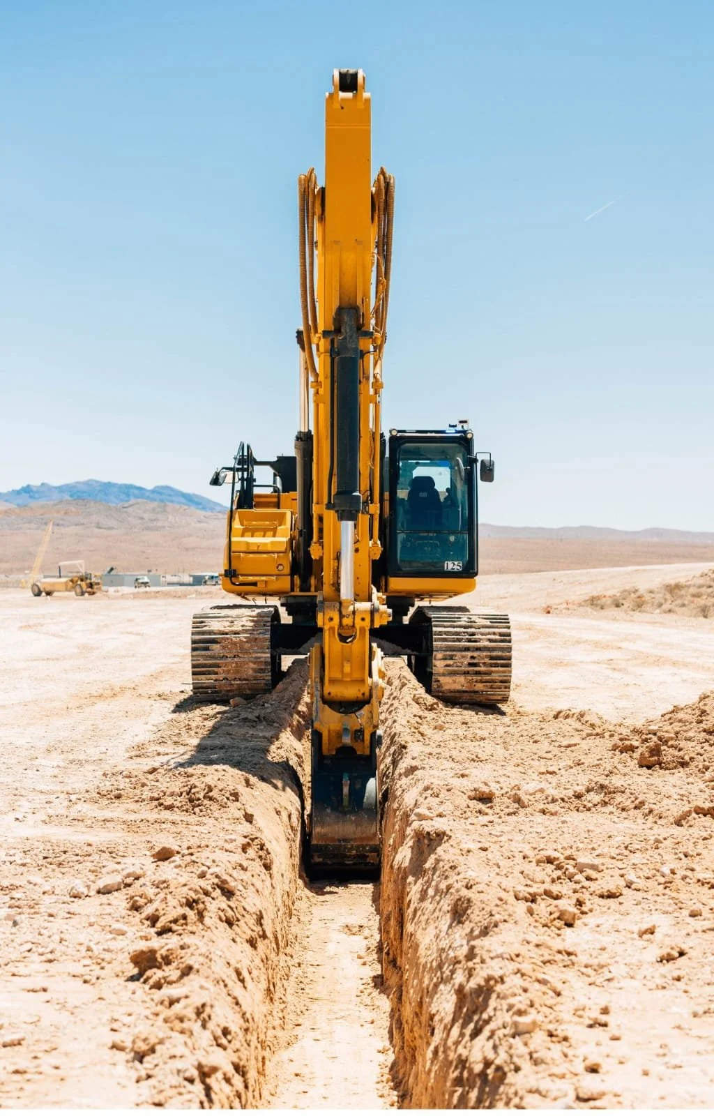 Yellow excavator digging a trench in a desert landscape.