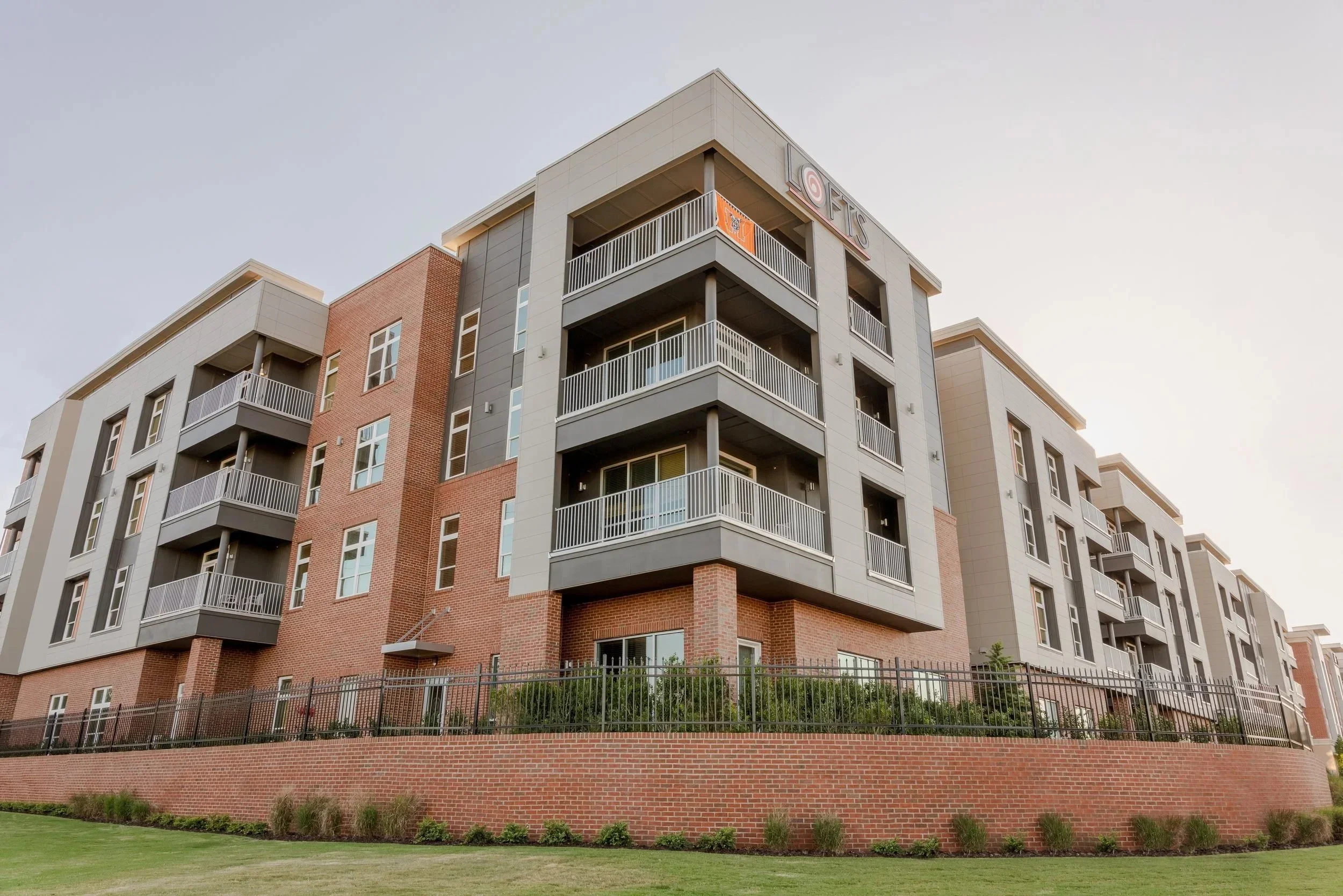 Exterior of Lofts at Mercer Landing II, an apartment building in Macon, GA near the Mercer University featuring 4 floors of 3-4 bedroom apartments with balconies overlooking a green space.