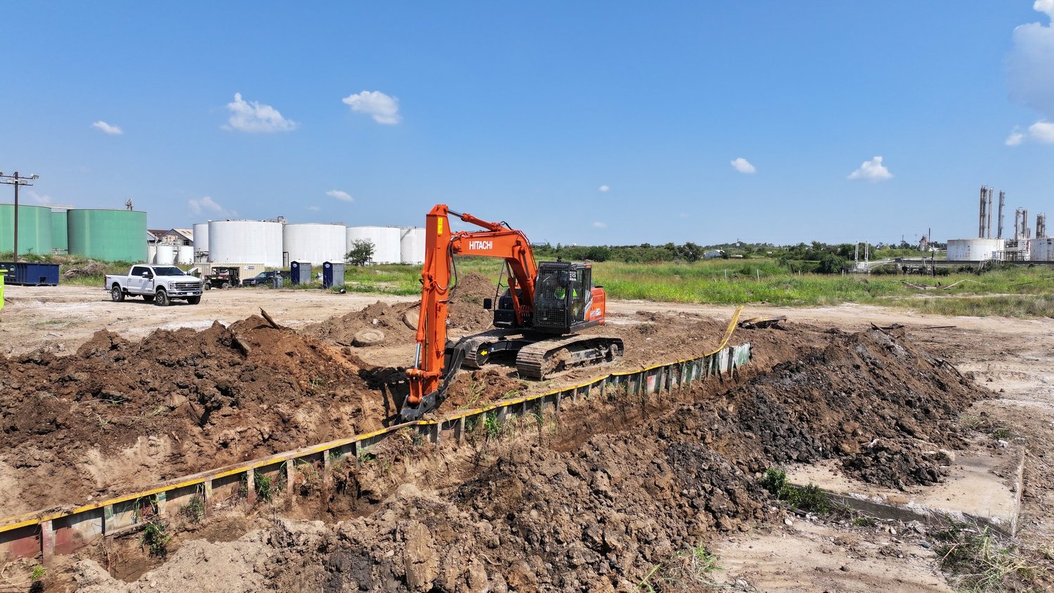 Excavator digging a trench beside a temporary retaining wall on an industrial site