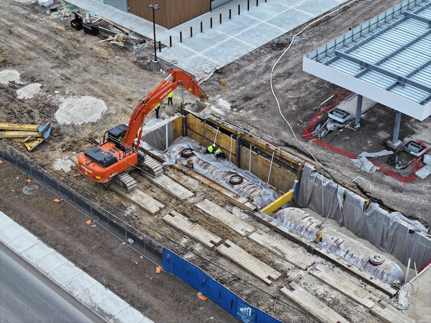 Excavator working beside a shored excavation on a commercial site, crew in hi-vis