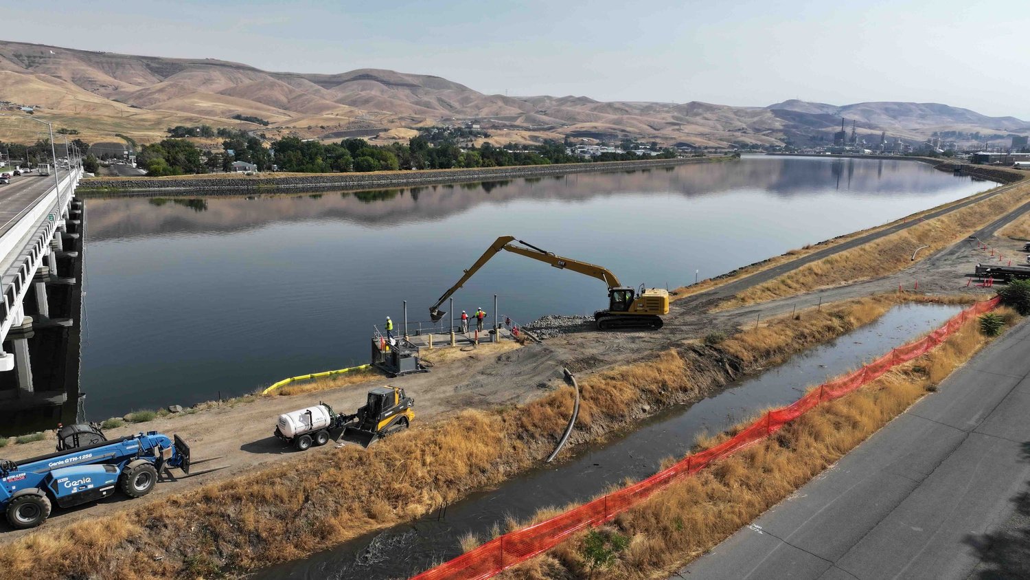 Long-reach excavator at the water's edge with a silt curtain in place on an outfall project