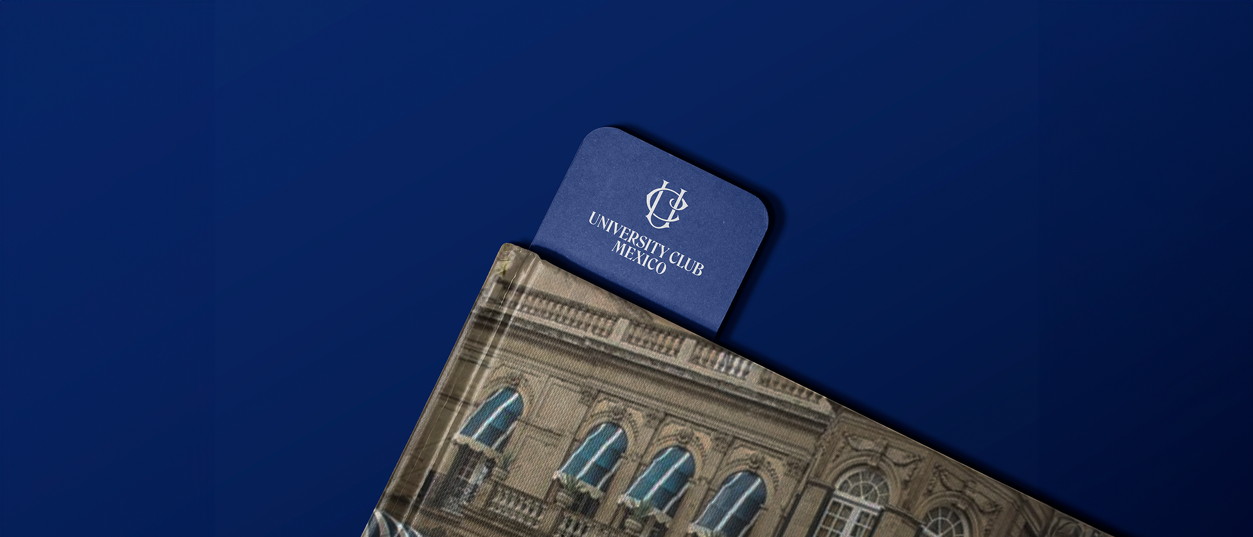 Blue card labeled 'University Club Mexico' partially inside a brochure with an architectural building on its cover, placed on a dark blue background.