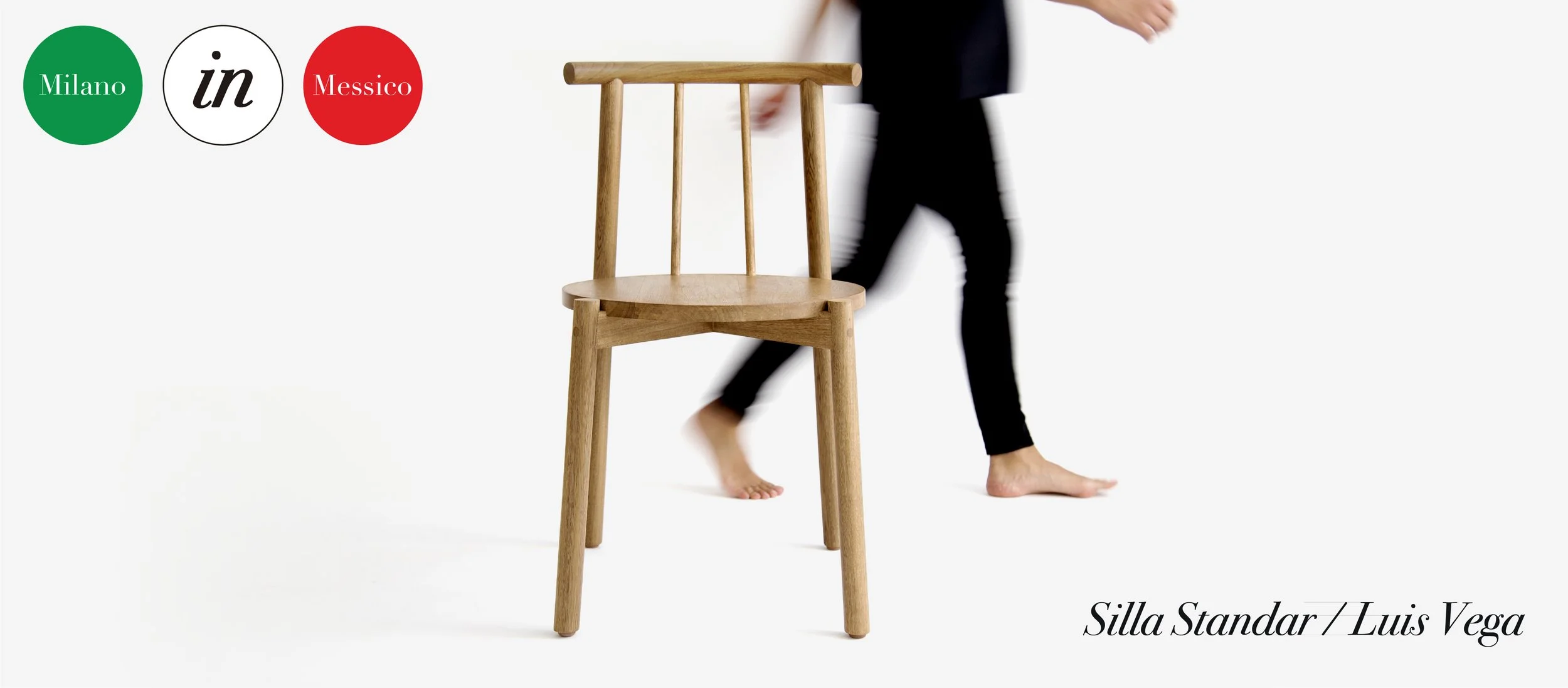 Una silla de madera de diseño sencillo llamado Silla Estándar por Luis Vega, con una persona de fondo caminando sin zapatos. La imagen tiene un fondo blanco y en la esquina superior izquierda hay un logotipo con círculos verdes, blancos y rojos que d