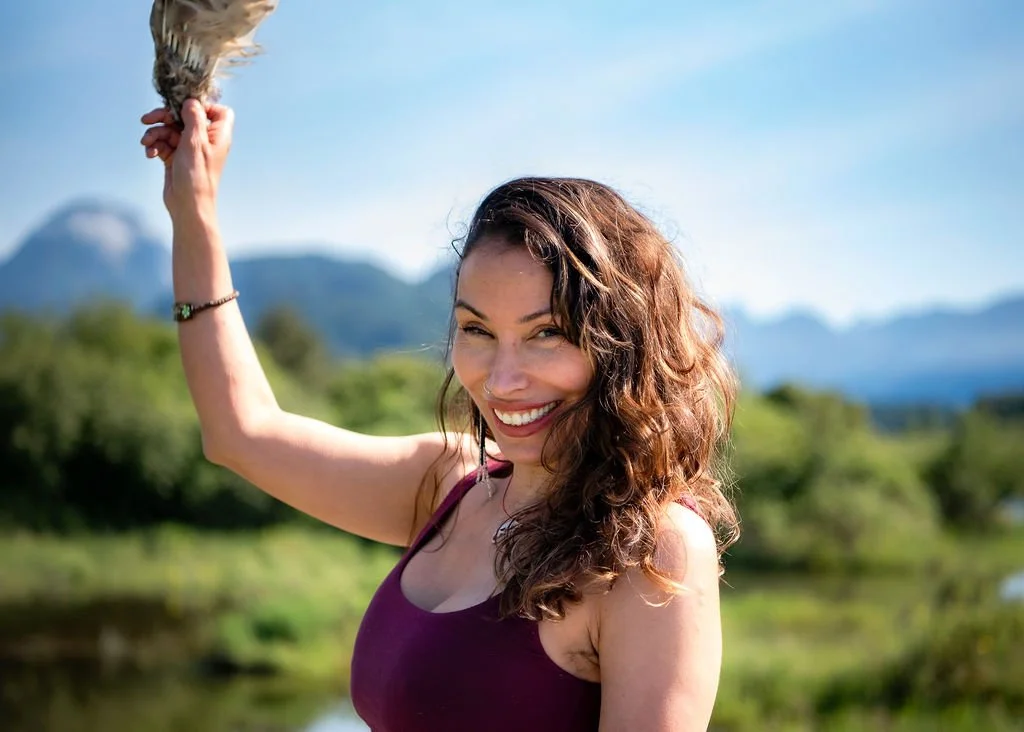 A woman outdoors holding a hawk on her hand, with mountains and a blue sky in the background.