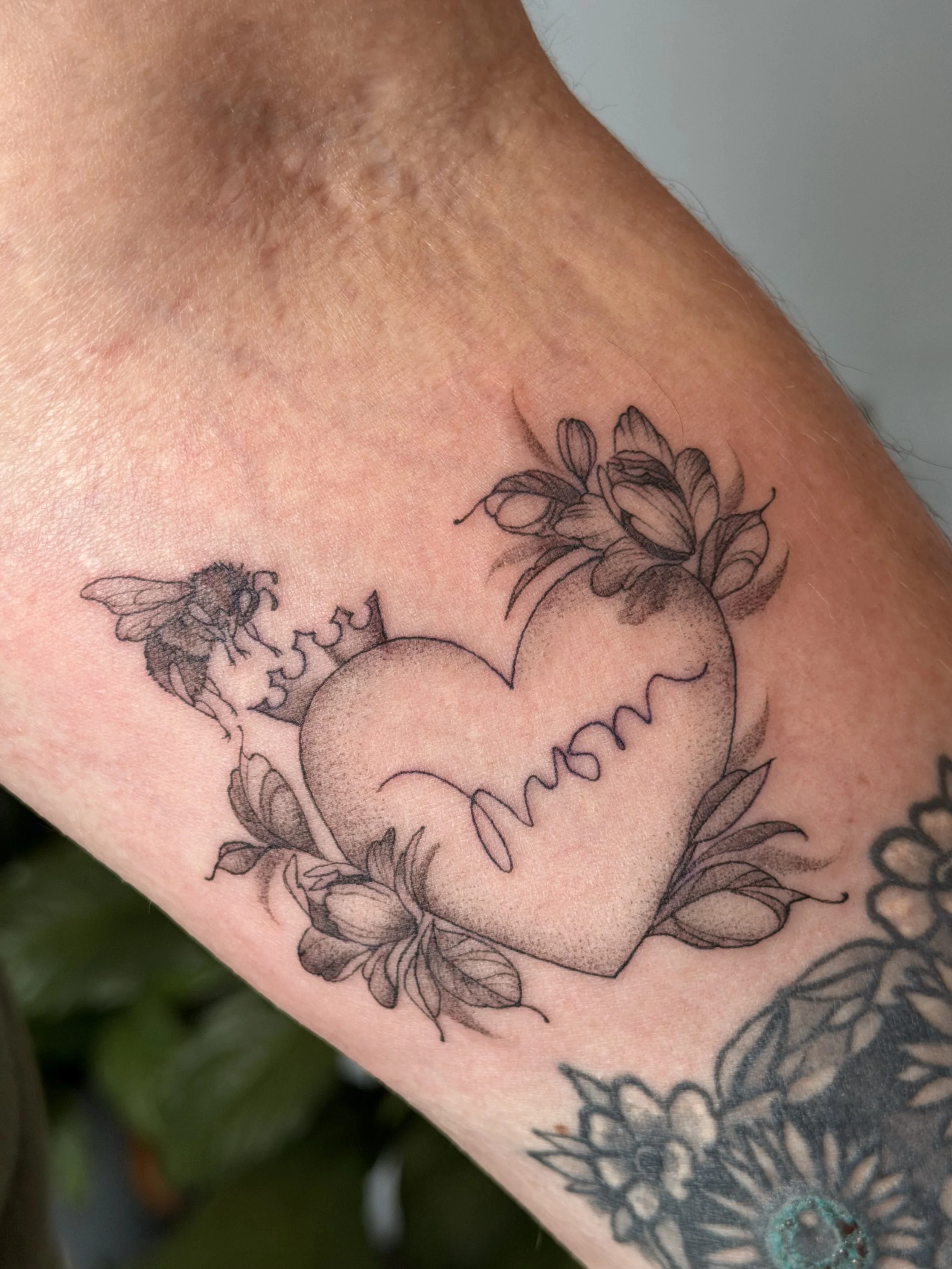 Tattoo of a heart with an ECG line pattern, surrounded by flowers, on someone's skin.