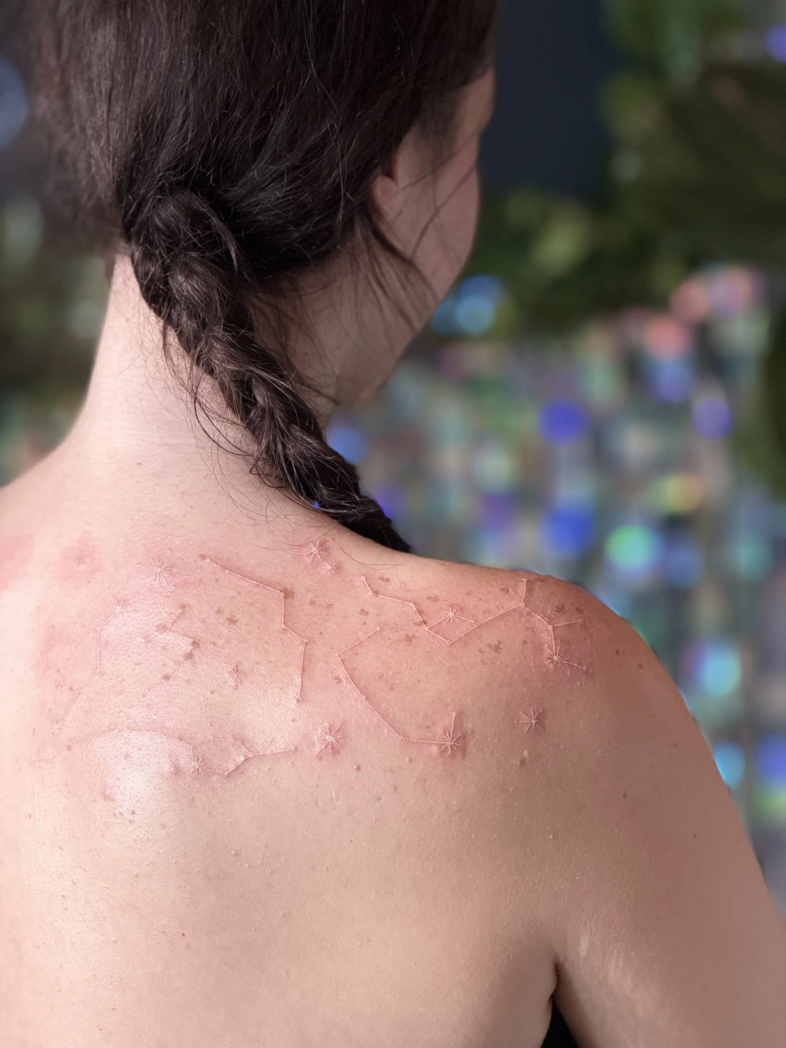 Close-up of a woman's shoulder and back showing skin with a constellation tattoo in white ink.