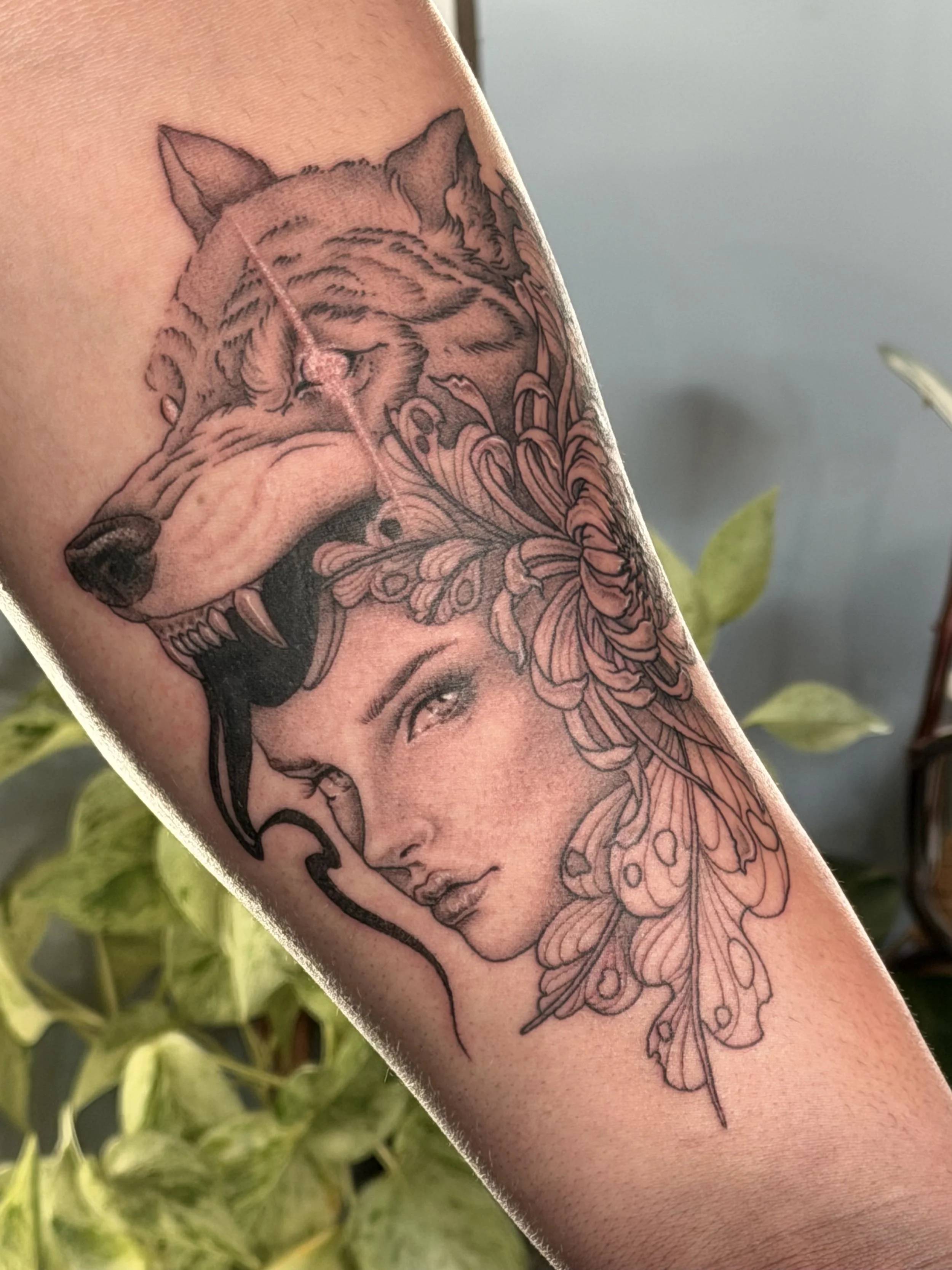 Tattoo of a wolf head and a woman's face with floral and feather elements.
