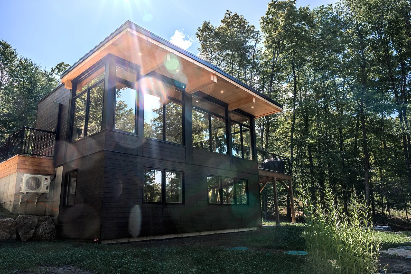 Façade moderne parfaitement intégrée à la forêt des Laurentides, offrant une atmosphère unique et lumineuse.