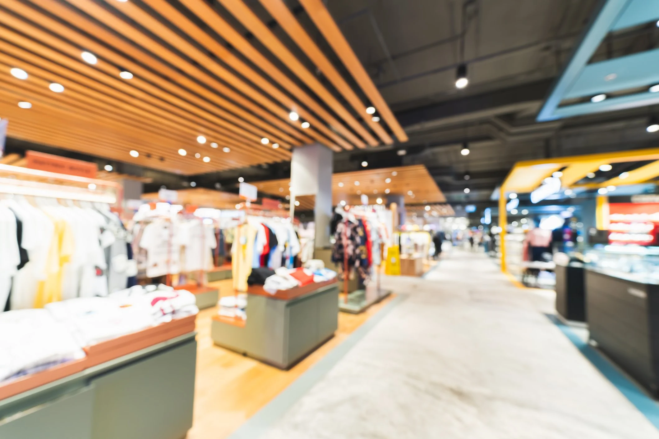 Blurred photo of a retail store with clothing displays, racks, and overhead lighting.