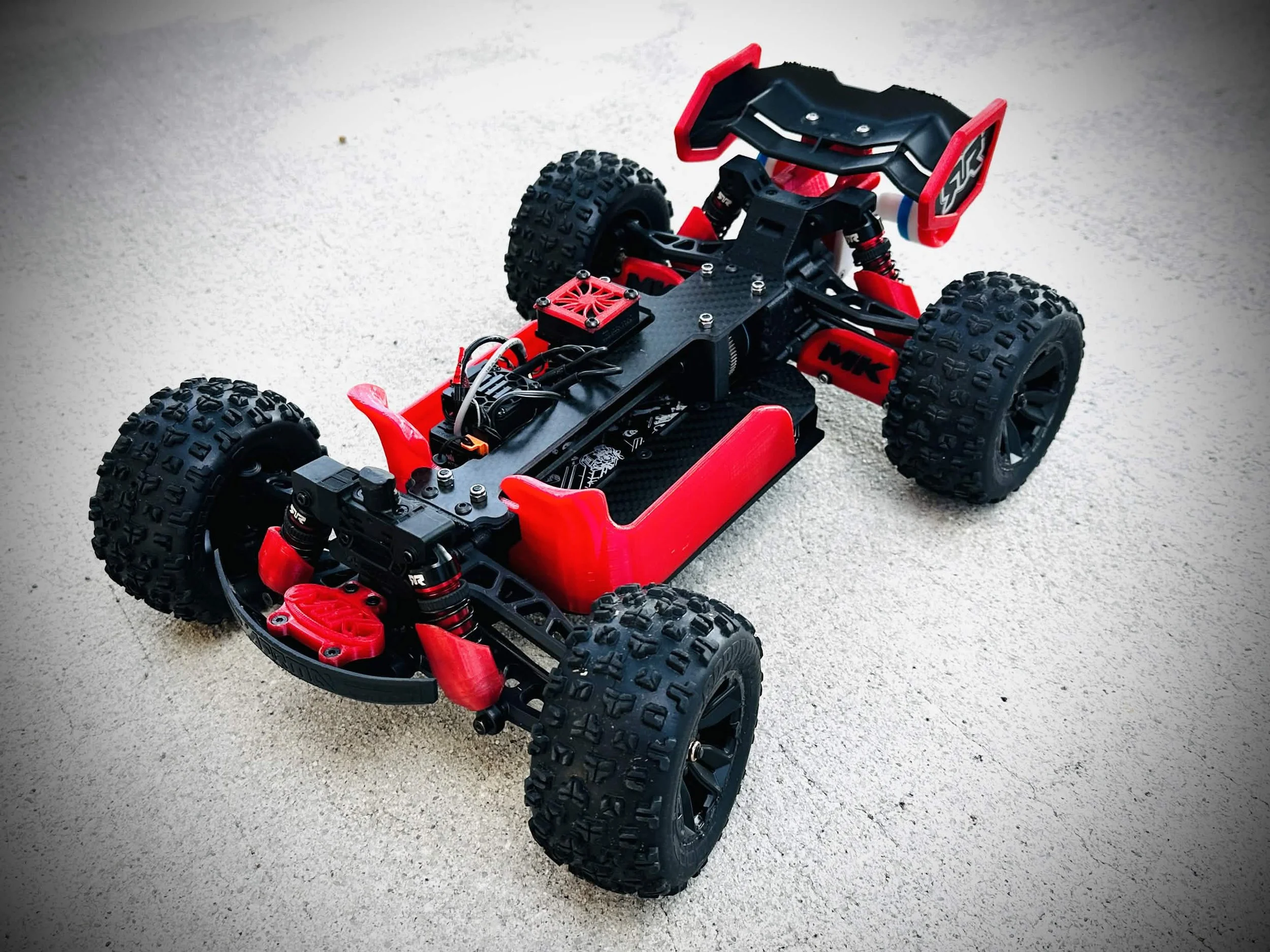 An electric remote-controlled off-road vehicle with large rugged tires and a sleek black and red body frame on a sandy surface.
