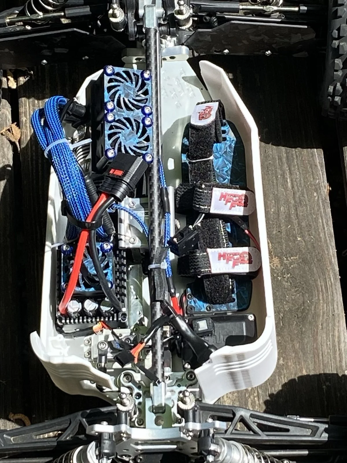 Close-up view of an exposed motorcycle or scooter chassis with visible electronic components, wiring, cooling fans, and straps for securing parts.
