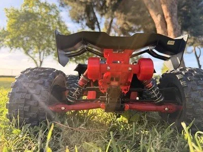 Close-up of a red remote-controlled off-road vehicle with large tires, sitting on grass with trees in the background.