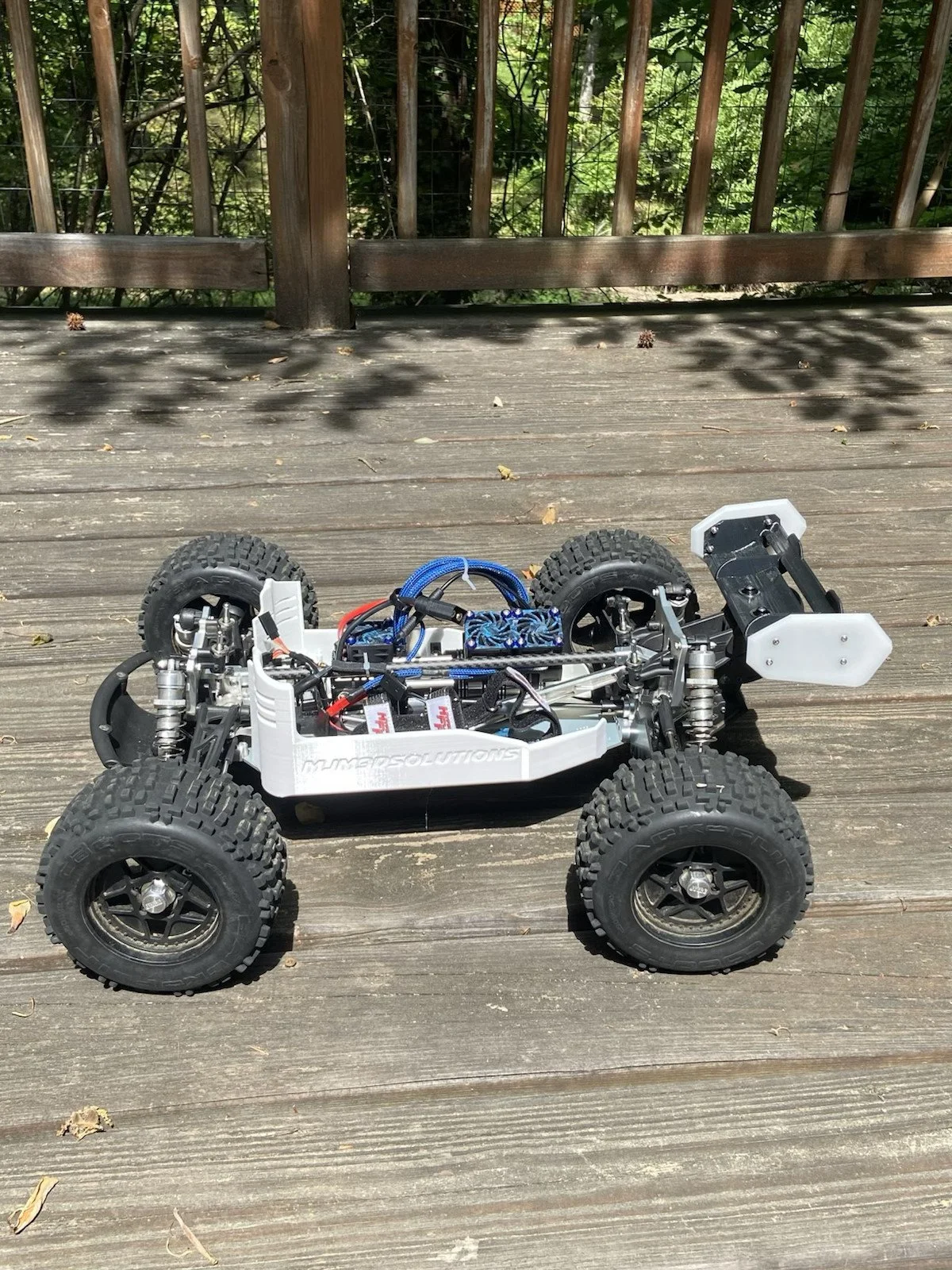 An off-road RC car with large tires and a white body shell on a wooden deck.