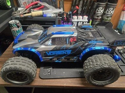 A blue and black remote-controlled off-road truck on a workbench surrounded by tools and supplies.