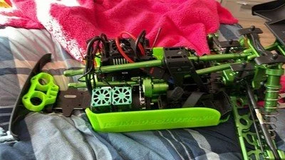 A partially assembled green remote control car chassis with exposed internal components, sitting on a bed with a pink blanket.