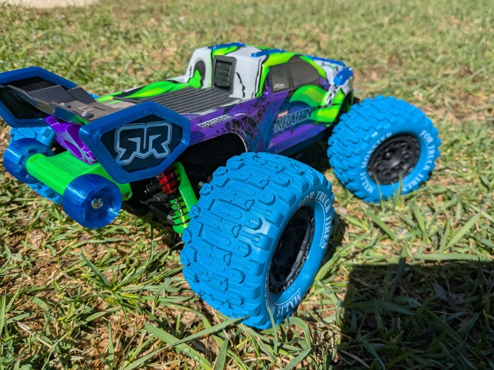 Remote control race car with green, purple, white, and blue colors and large blue tires on grass.