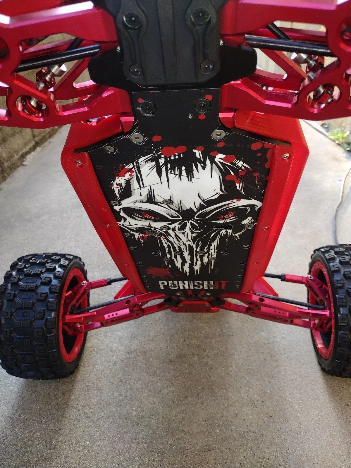 View of a small remote-controlled car with a red frame, black and white graphic on the underside, and large off-road tires.