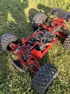 A red remote-controlled off-road vehicle with large tires and a visible chassis, lying on grass.