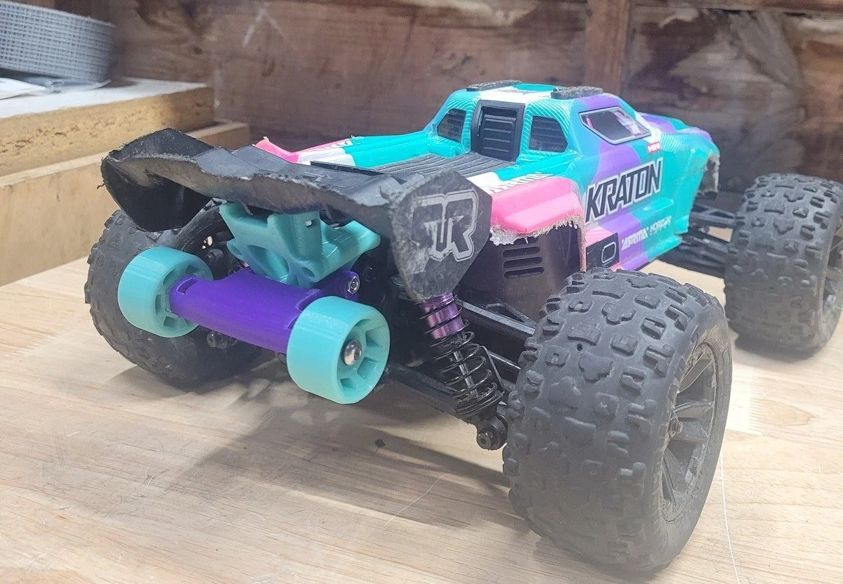 A colorful remote-controlled toy truck with large off-road tires, suspension, and a custom body, placed on a wooden surface.