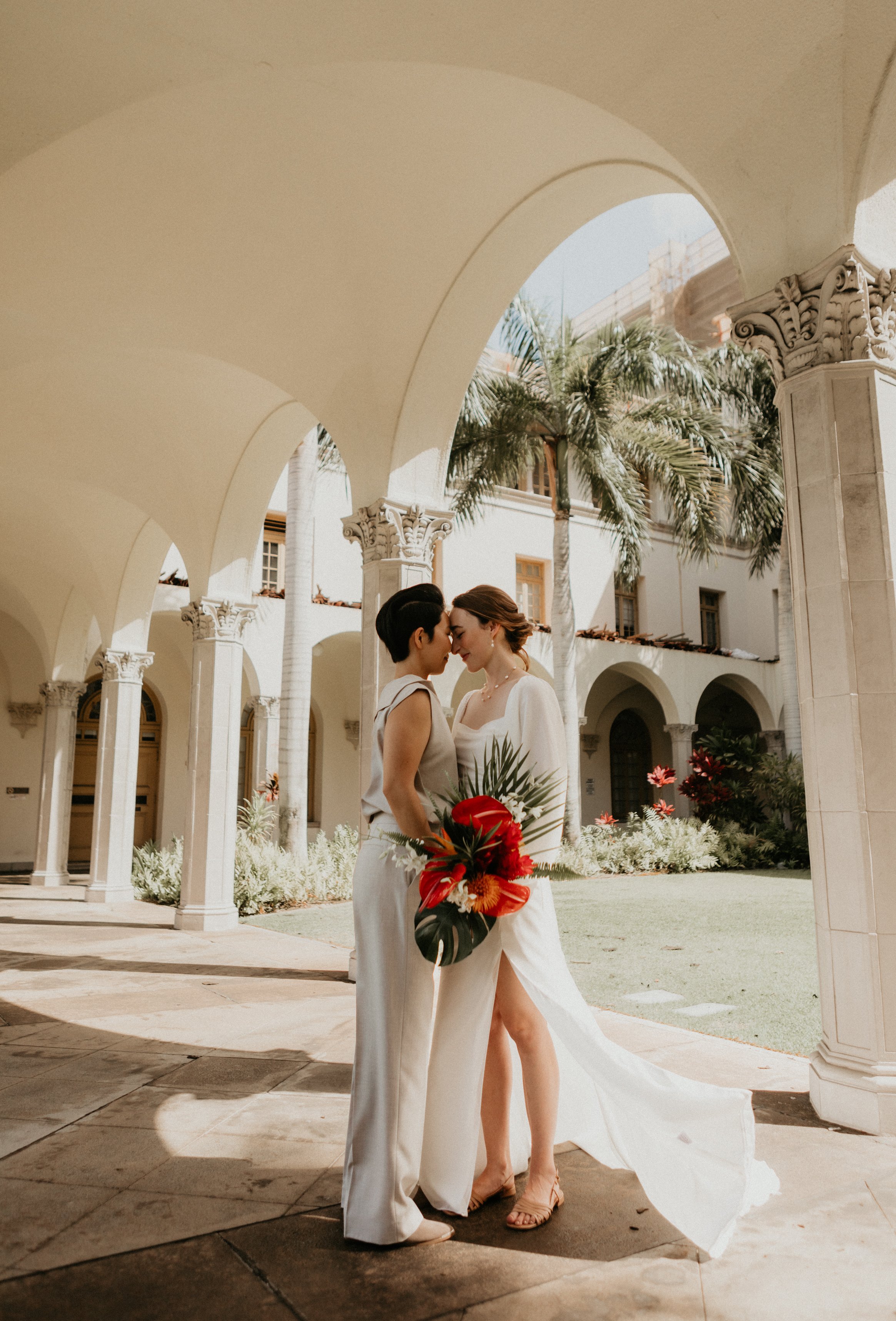 A bride with dark, wavy hair in a white gown holding a cascading bouquet of white flowers in hawaii taken by aloha media weddings