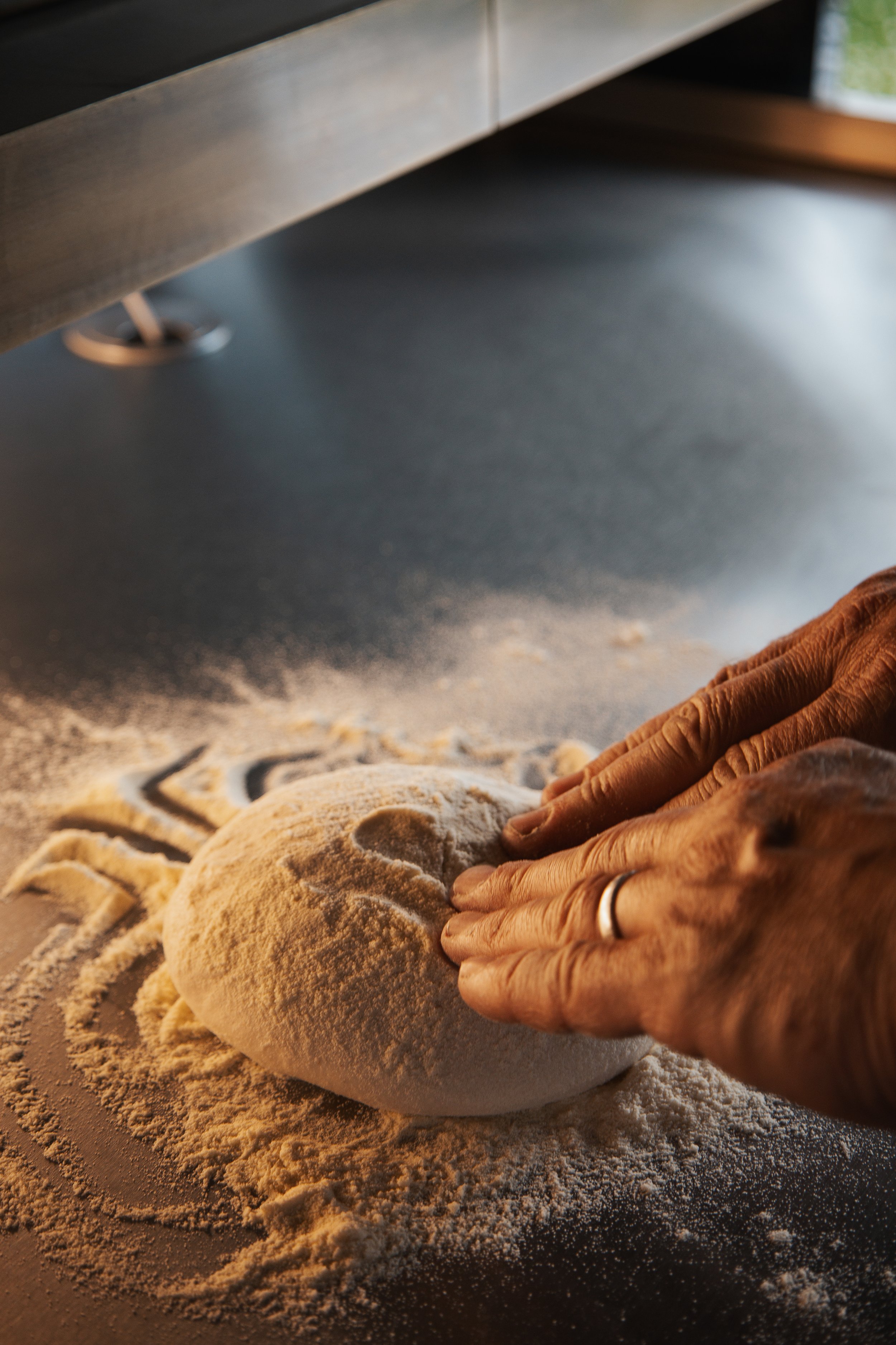 Hands shaping dough on a floured surface with the word 'pizzeria' partially visible underneath.