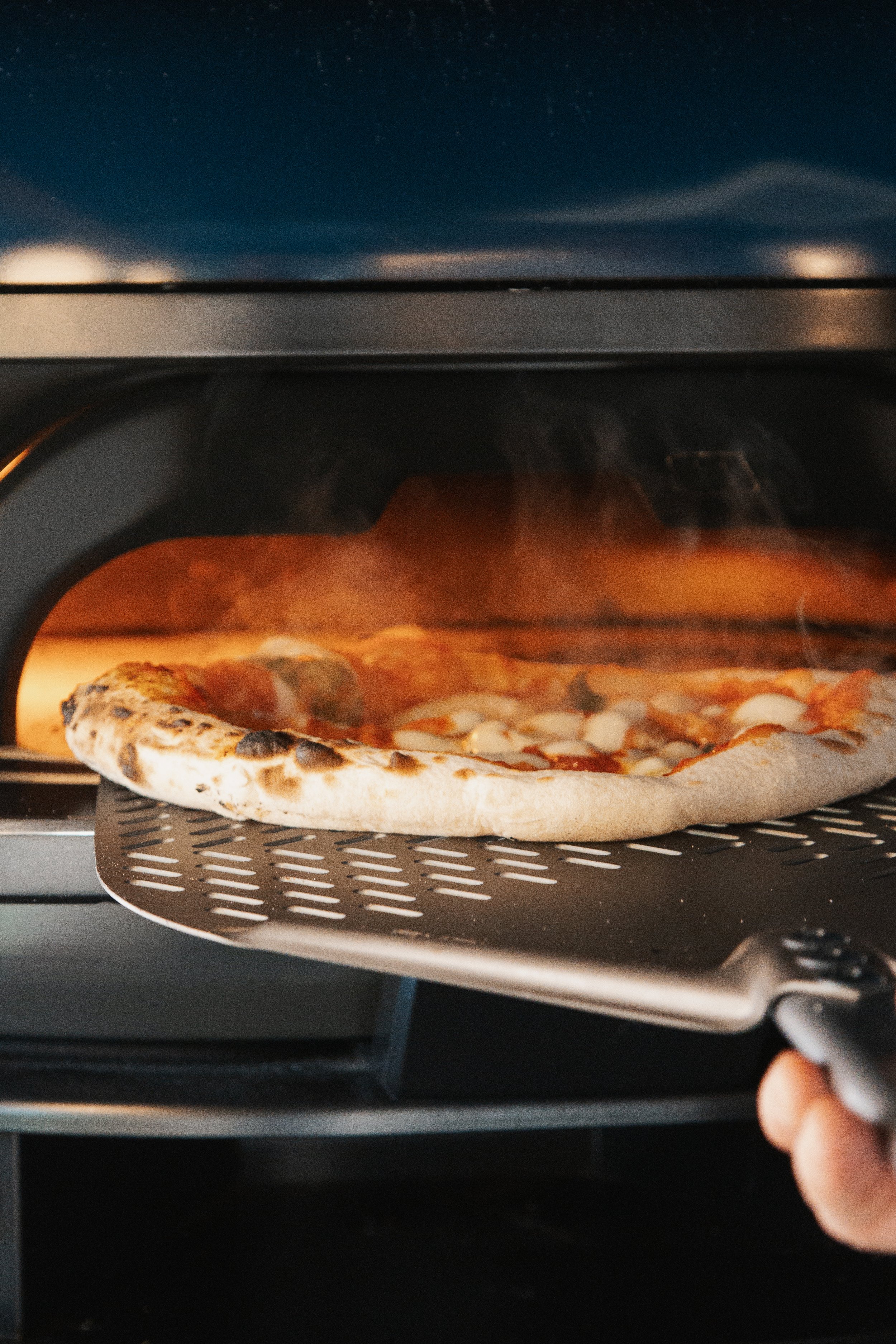Pizza being taken out of an oven with a pizza peel.