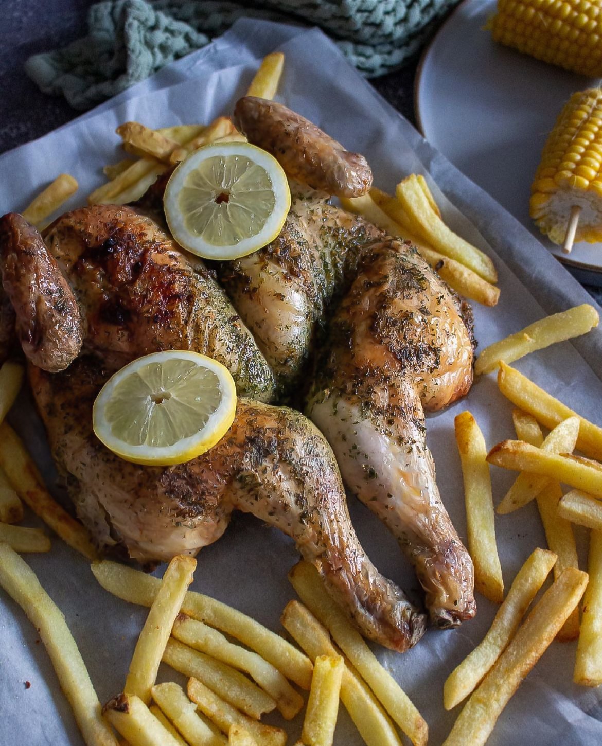 Roasted chicken with lemon slices, French fries, and corn on the cob.