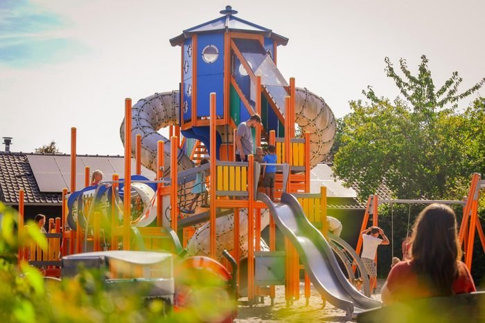 Kleurrijke speeltuin met glijbanen en klimtoestellen waar kinderen en ouders samen genieten van een zonnige dag buiten.