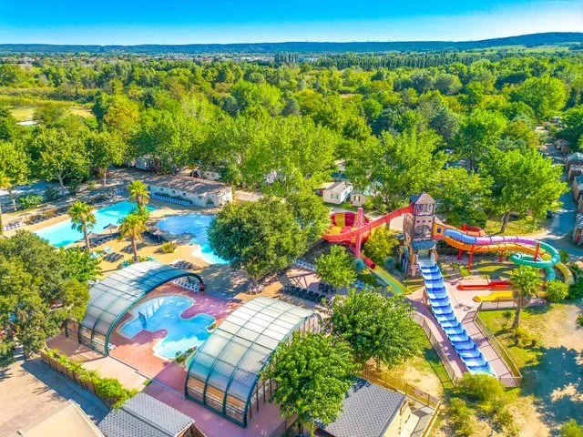 A water park surrounded by lush green trees with multiple water slides, a splash pad, and pool areas under a clear blue sky.