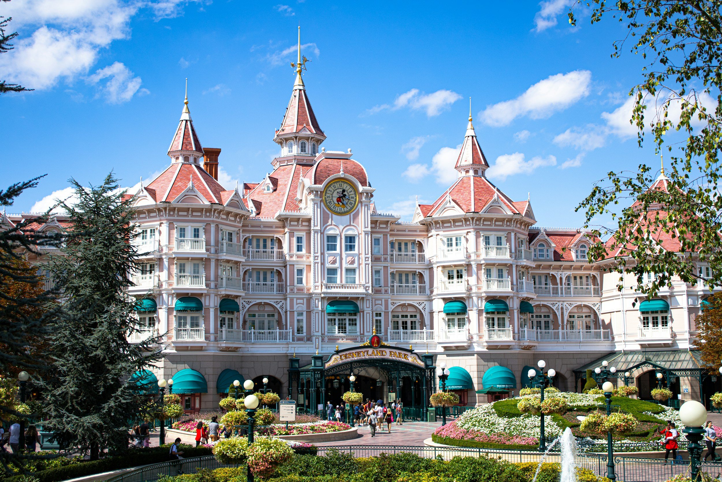 The Disneyland Park entrance with a pink and white Victorian-style castle, surrounded by landscaped gardens and visitors