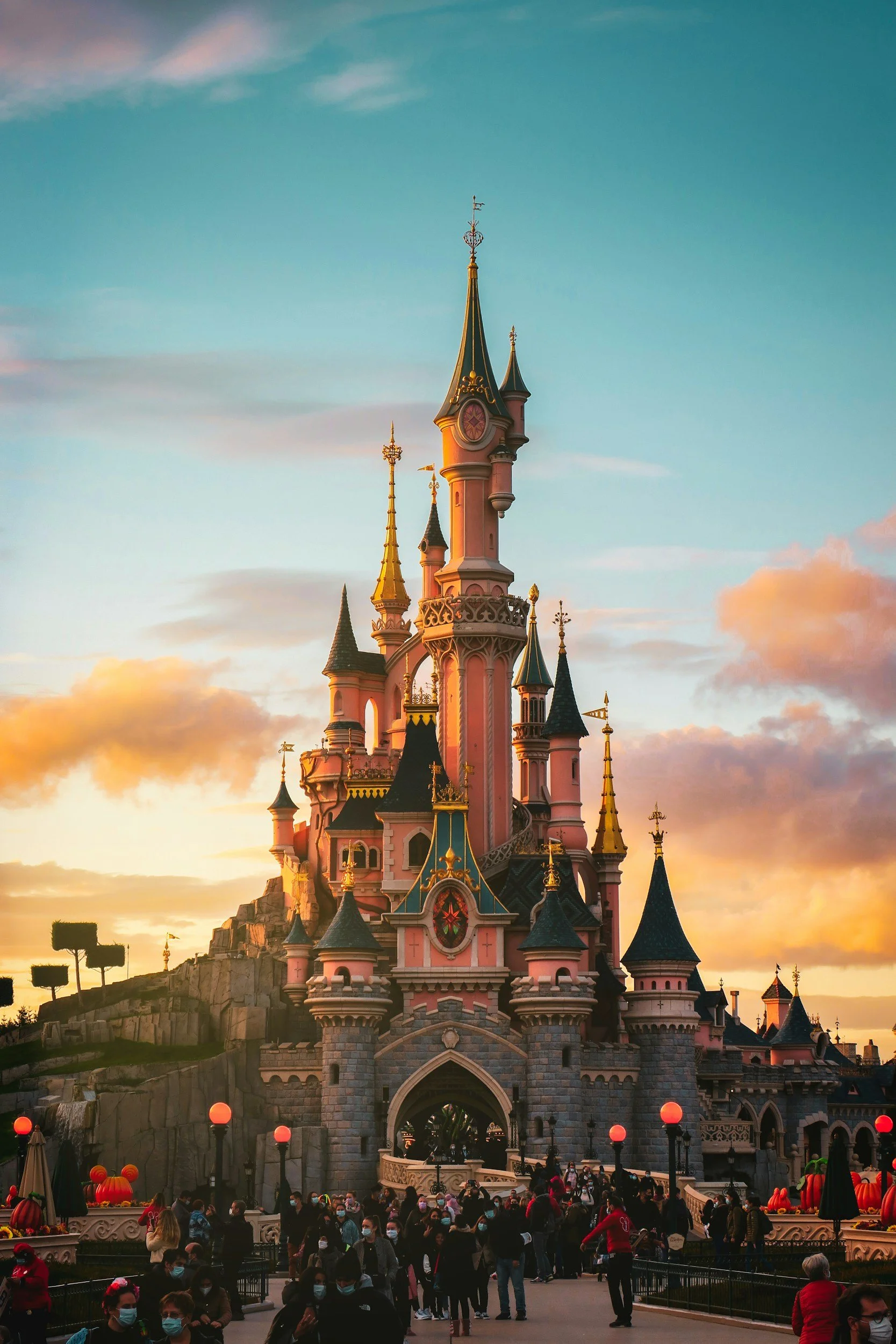 Sleeping Beauty Castle at Disneyland during sunset with crowds of visitors in front.