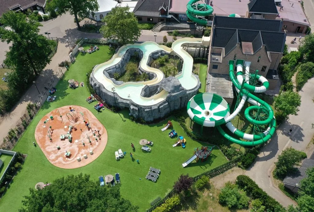 Aerial view of a water park with lazy river, water slide, play area, and surrounding green lawn and trees.