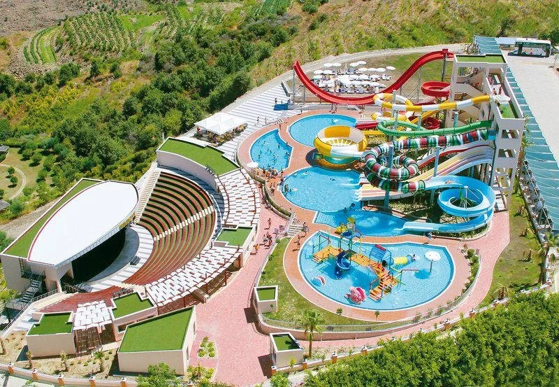 Aerial view of an outdoor water park with water slides, pools, and a concert stage, surrounded by greenery.