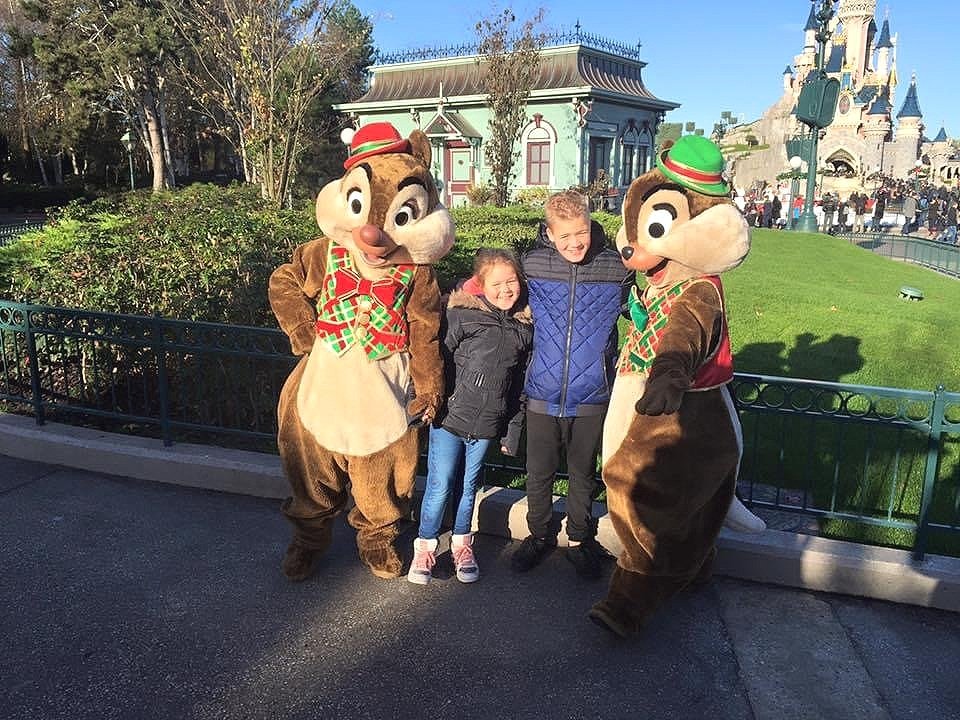 Two children posing with two characters dressed as chipmunks at Disneyland, with a castle in the background.