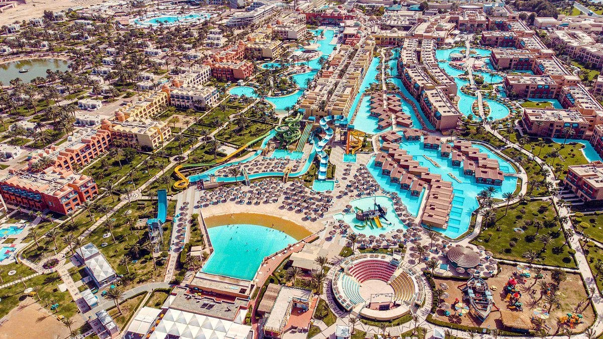 Luchtfoto van een luxe waterpark met lazy rivers, waterglijbanen, zwembaden en liggedeeltes tussen palmbomen en resortgebouwen