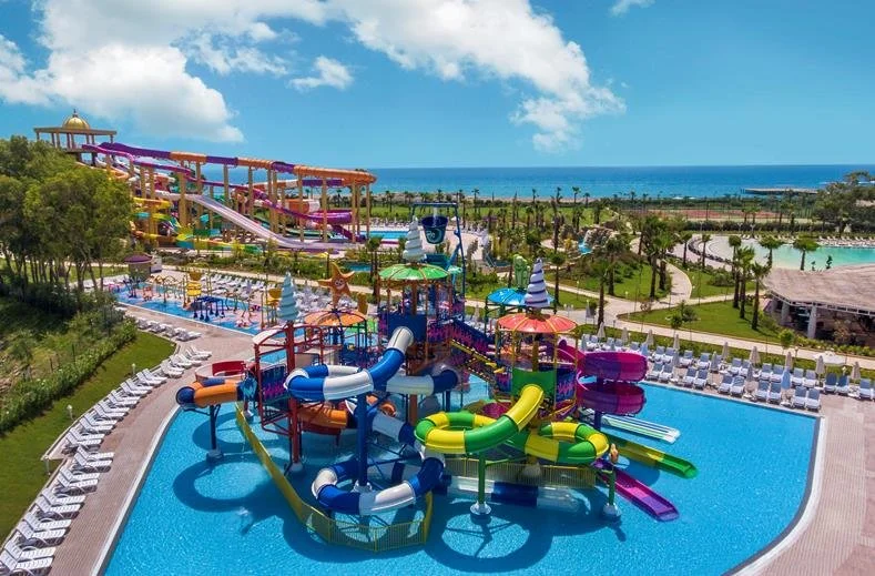 Kleurrijk waterpark met meerdere waterglijbanen, een zwembad en ligbedden, gelegen aan zee met uitzicht op de oceaan. Dit beeld past perfect bij een all inclusive resort en een zonvakantie met kinderen waar waterpret centraal staat.