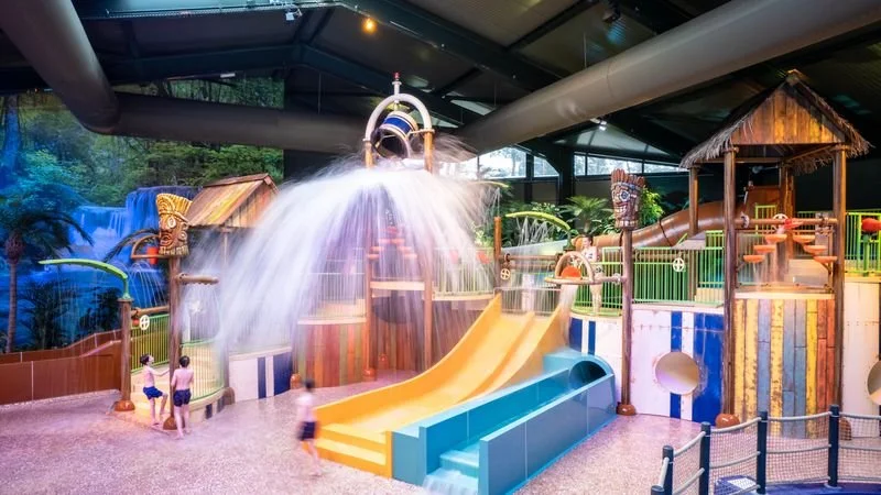 Indoor water playground with water slide, water features, and tropical-themed structures.