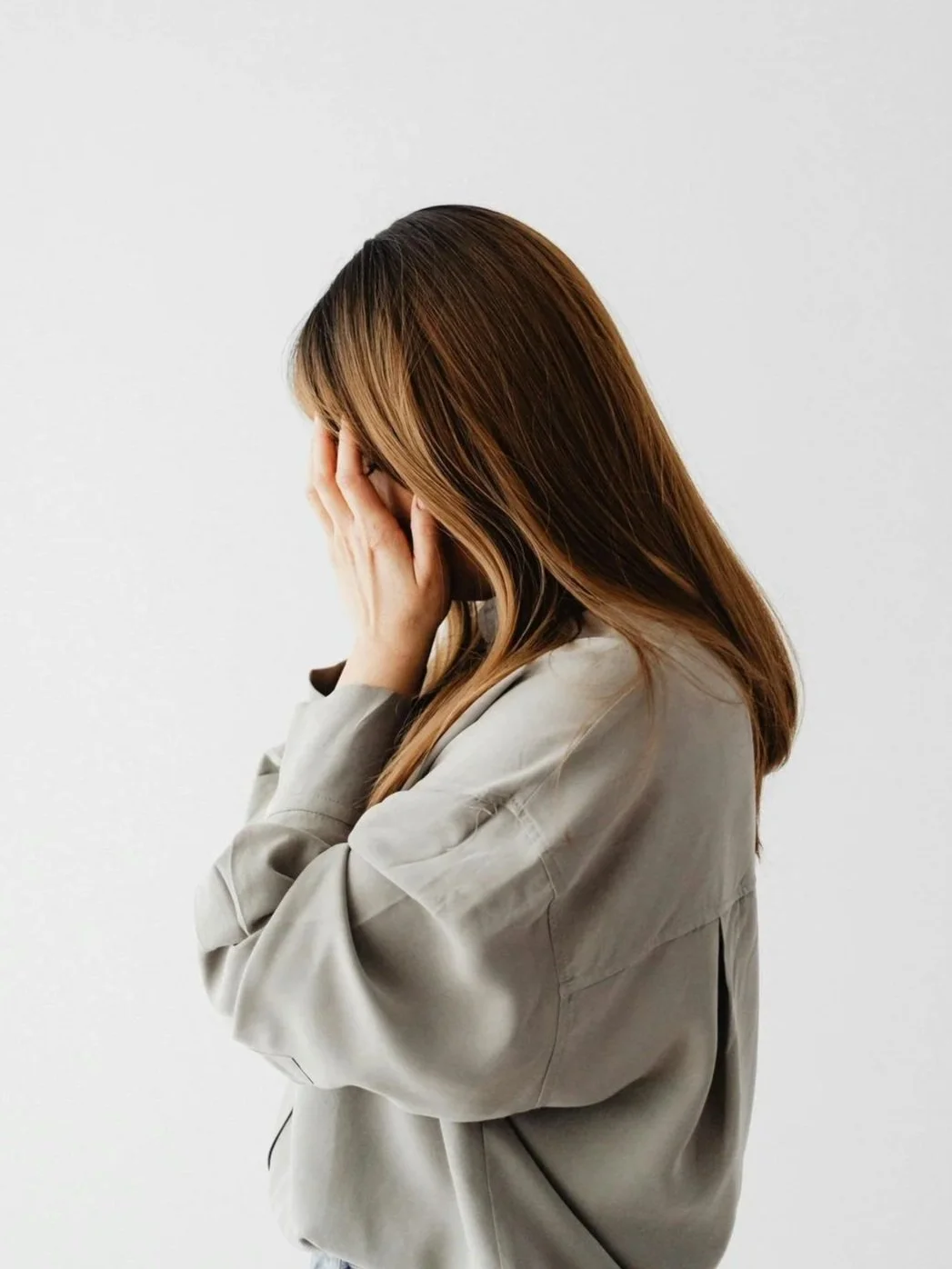 woman in taupe top with hands cover face facing to the side
