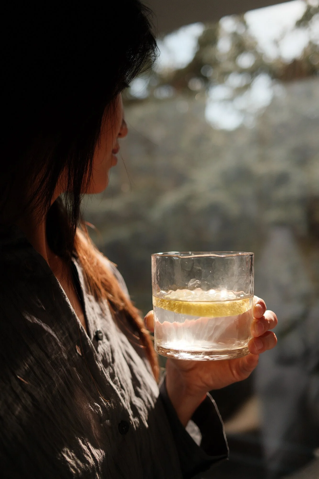 woman lookin out to nature holding glass of water with lemon
