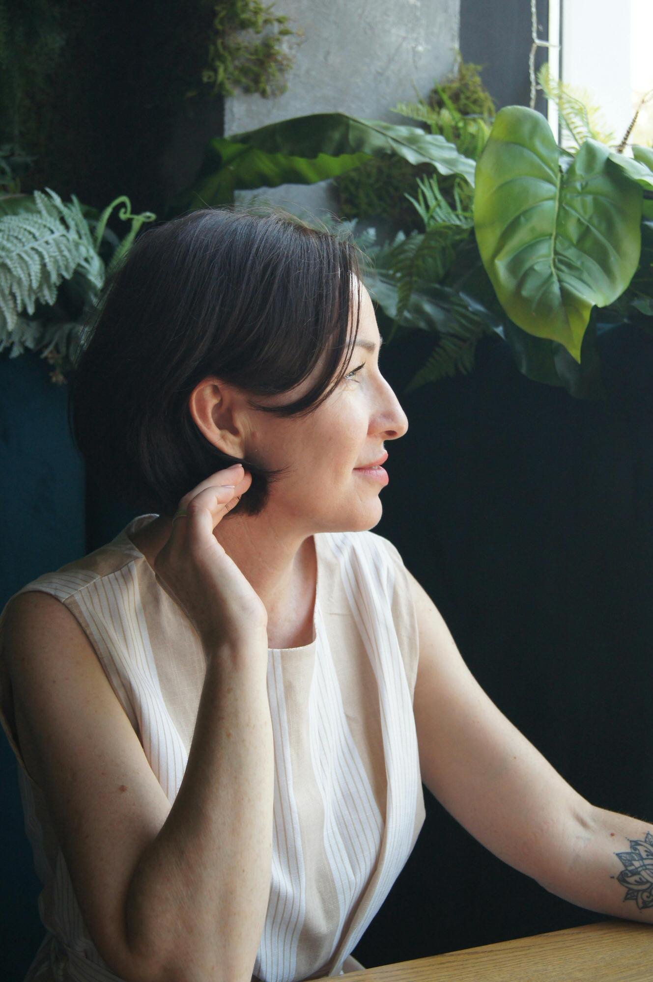 woman with short black hair looking off to the side slight smile green plants behind her