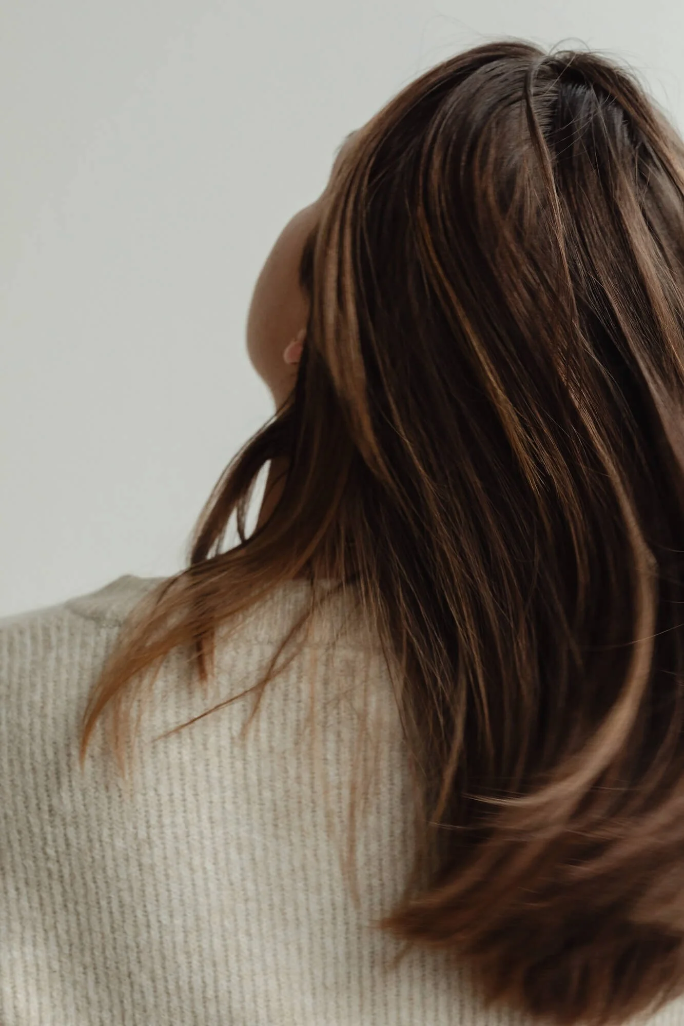 woman from back with white sweater head tilted slightly up and long brown hair