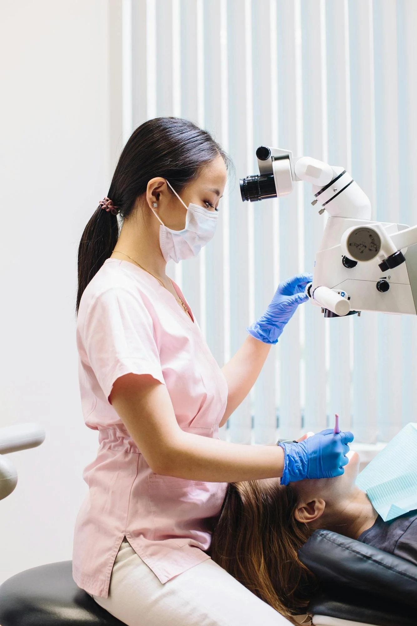 dentist in pink scrubs, blue gloves examining patient