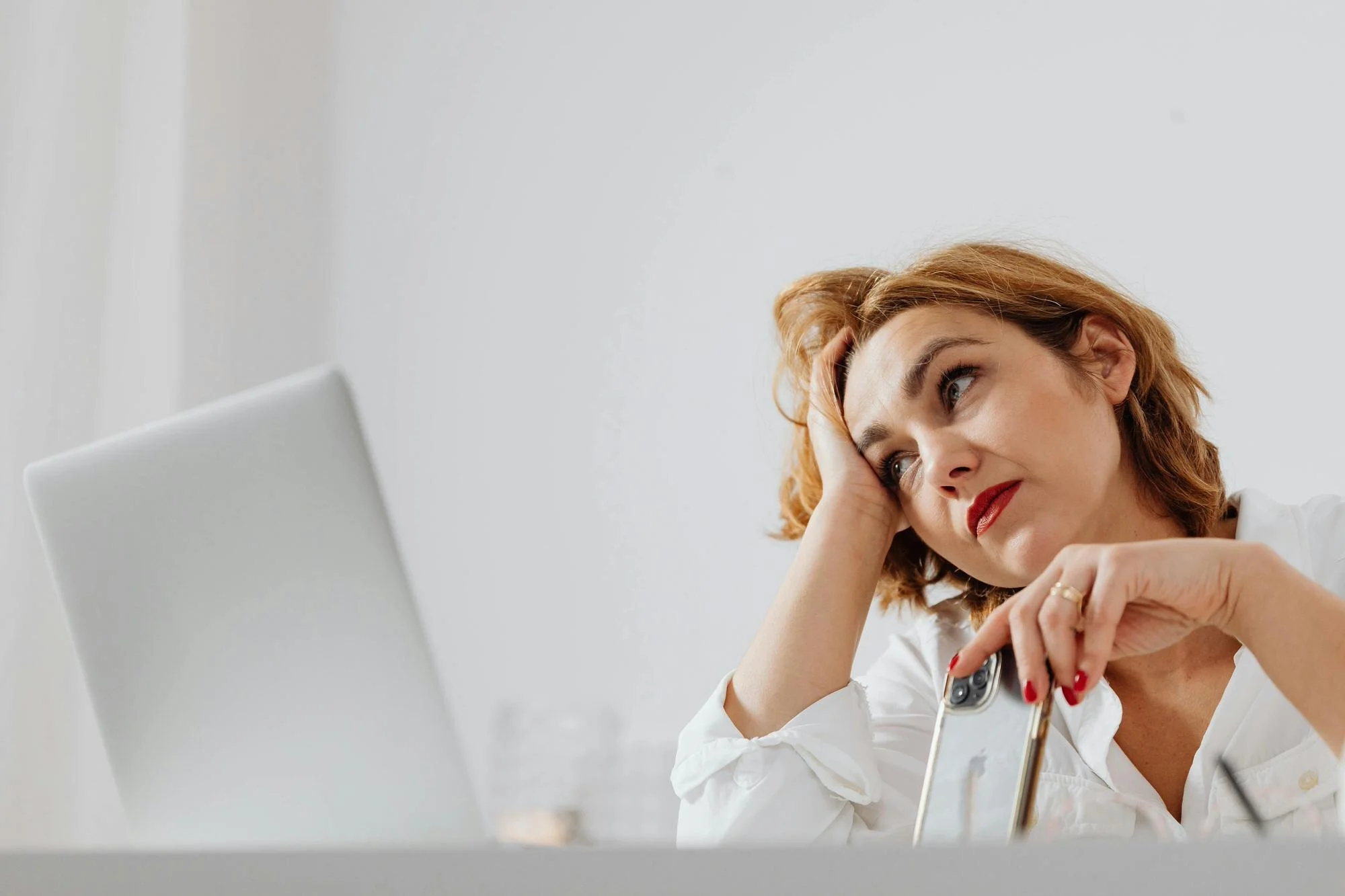therapy for high achievers - woman with phone in one hand and leaning head in other hand looking stressed or frsutrated