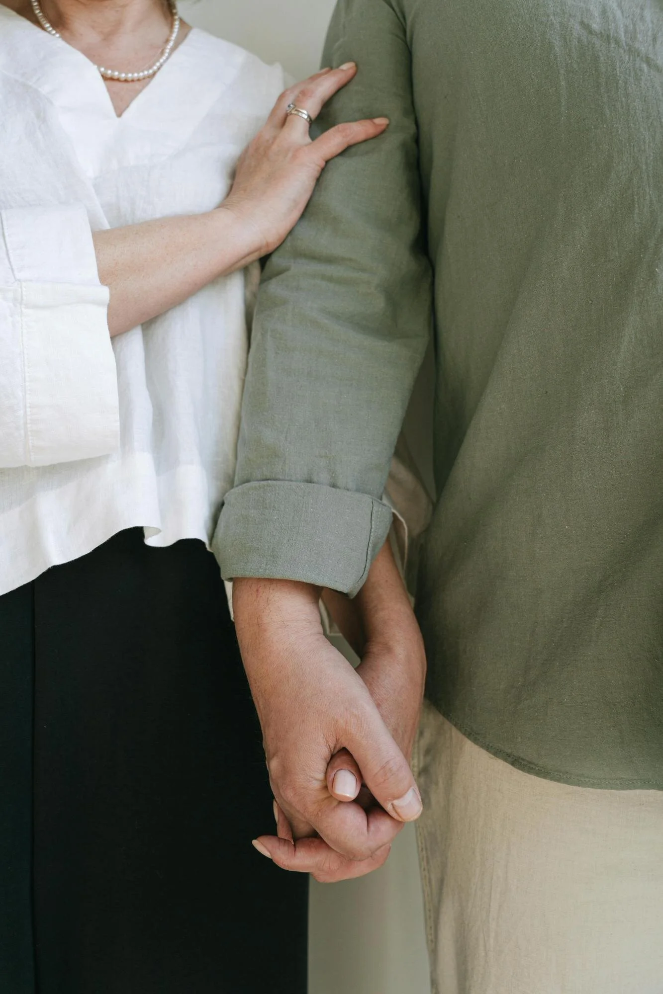 couple standing and holding hands - man in kahaki pants and olive shirt and woman in black pants and white blouse