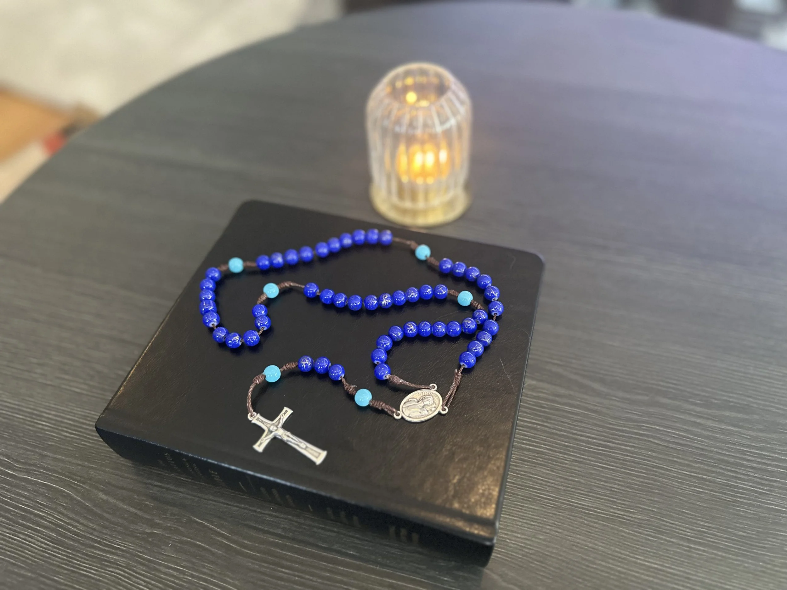 Hand-knotted rosary featuring deep blue "Hail Mary" beads and light blue "Our Father" accent beads on a brown cord with a silver Saint Sebastian centerpiece.