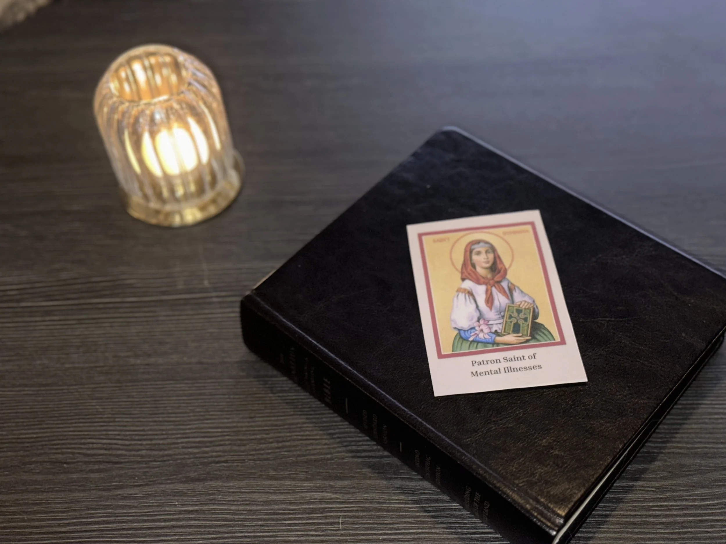 St. Dymphna prayer card featuring a colorful illustration of the saint holding a book and a flower, labeled "Saint Dymphna, Patron Saint of Mental Illnesses."