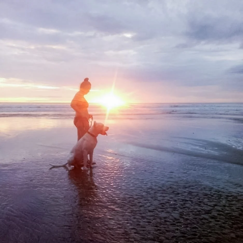 Tamara Doering, integrative pelvic health practitioner, standing on a sandy beach at sunset with her dog, Ademir, in Playa El Coco, Nicaragua, supporting women's pelvic care in Calgary, AB and San Juan Del Sur, Nicaragua